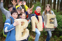 Kinder stehen im Wald mit großen Buchstaben aus Holz B, N und E