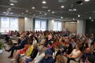 Viele Personen sitzen in einem Veranstaltungssaal.