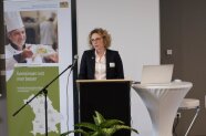 Frau am Rednerpult spricht in ein Mikrofon.