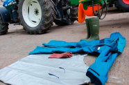 Schutzanzug, Handschuhe, Brille und Plane liegen auf Boden vor Traktor